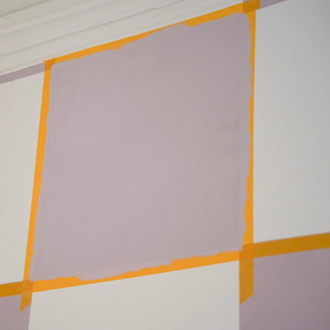 An einer Wand ist mit Abklebeband ein Quadrat abgeklebt und innerhalb des Quadrats wurde mit einer Wandfarbe gestrichen. 