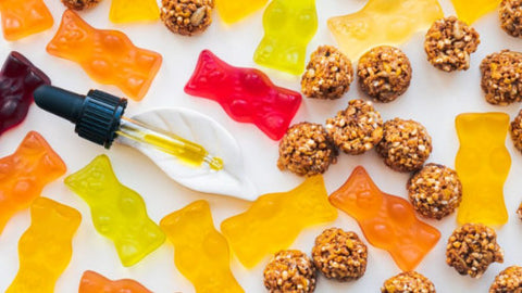 What Are The Best CBD Edibles I Can Take For My Tooth Pain? (White background with red, orange, and yellow CBD edibles with a CBD Oil dropper that has CBD oil in it and granola laid across the CBD edibles