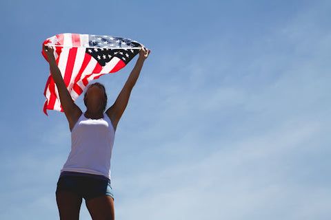 Woman holding an American flag above her head with a blue sky in the background