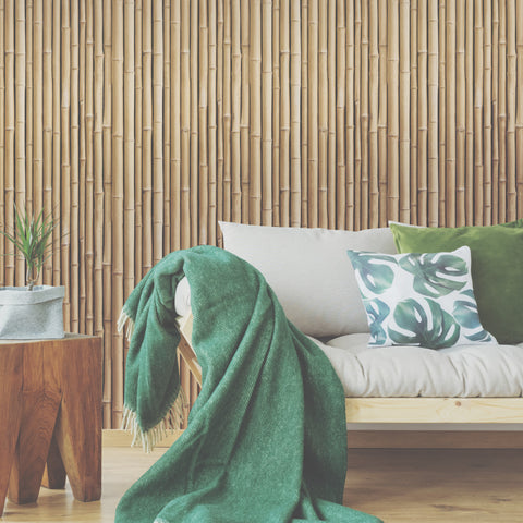 Tan Bamboo RoomMates Peel and Stick Wallpaper behind a beige couch with a green throw blanket and a wooden side table with a plant.  