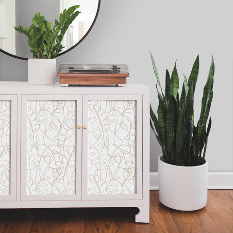 White/Taupe RoomMates Peel and Stick Wallpaper in-between neutral color shaker style cabinet doors pictures as an entry way table decorated with plants and a black framed circle mirror behind and a record player sitting on top.  