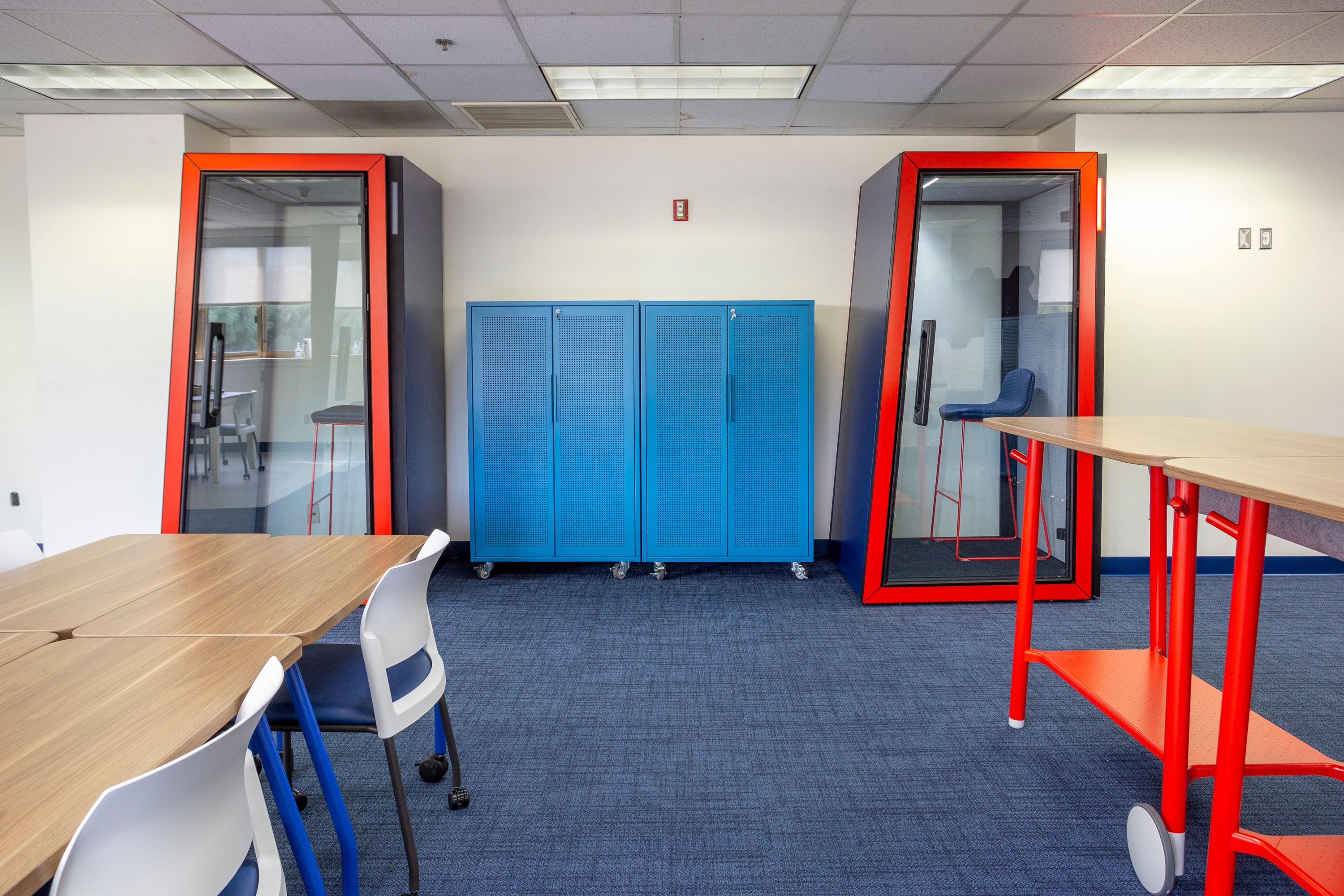Teacher workroom with tall storage cabinets, standing and sitting desks, and phone booths.