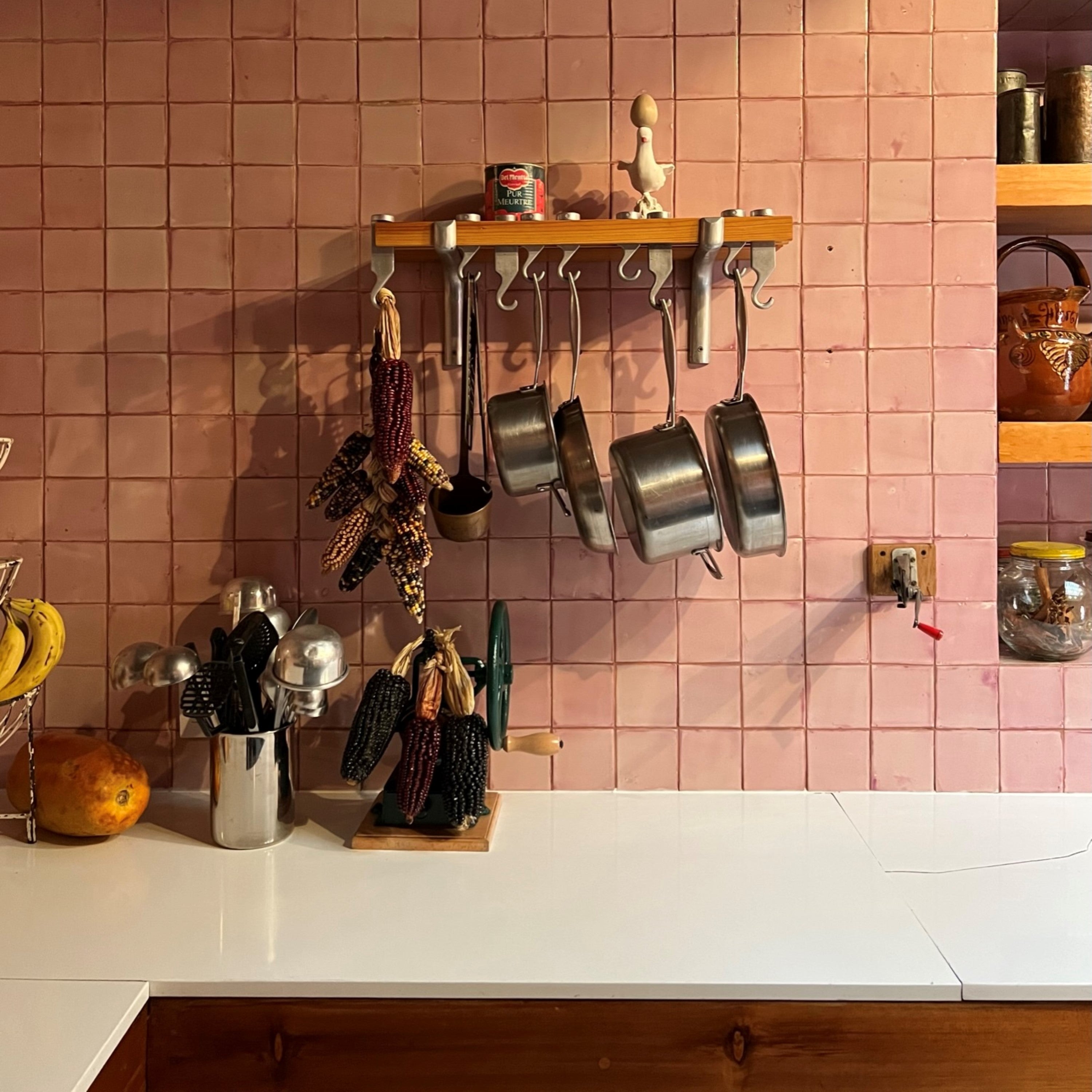 Photo of pots and pans hanging in a kitchen with a variety of colorful corn along a tiled wall