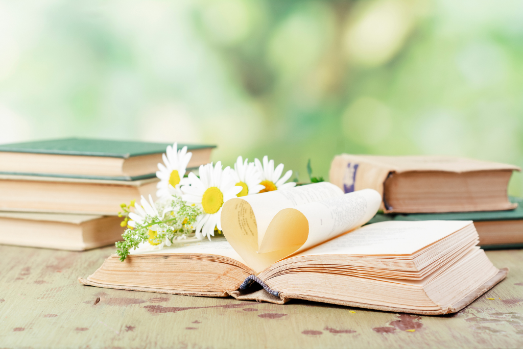 An open book with pages forming a heart shape, surrounded by flowers.