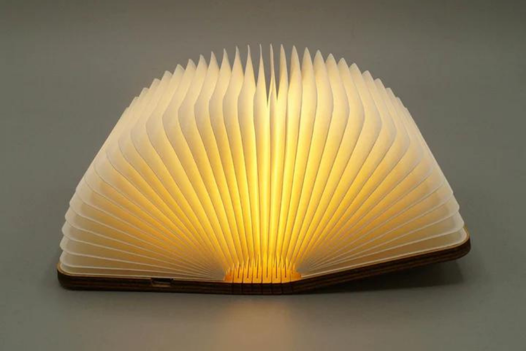 An illuminated book-shaped lamp opened on a dark background.