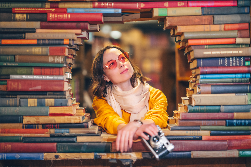 A person peering through a circle of stacked books with a camera in hand.