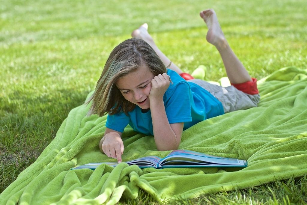 Child engrossed in reading on a blanket outdoors, embodying Once Upon a Book Club's encouragement of reading habits.