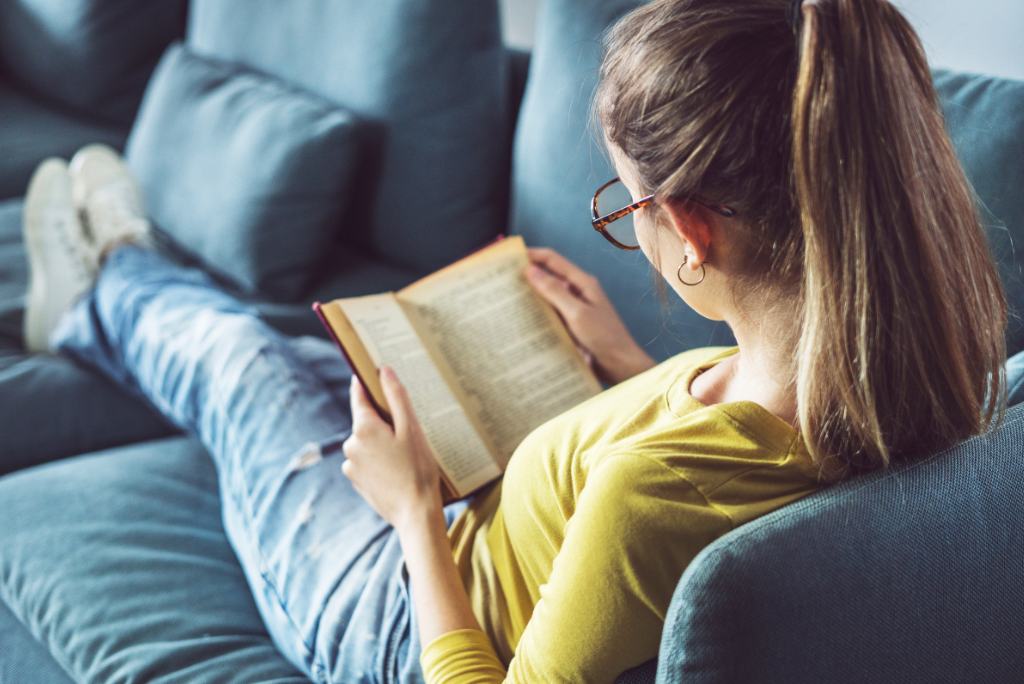 A person lounging on a couch, engrossed in reading a book.