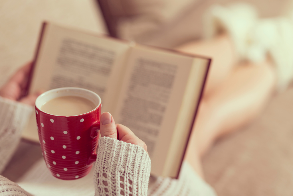 Hands holding a book and a polka-dotted red mug, suggestive of a cozy reading time