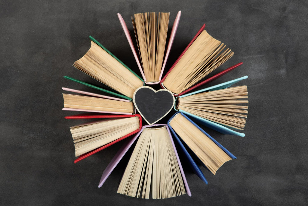 An array of hardcover books fanned out to form a heart shape on a dark surface, celebrating the love for reading and the sharing of knowledge.