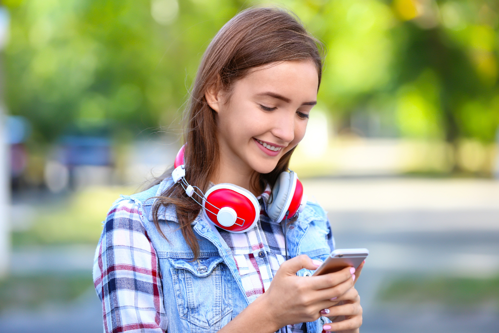 A happy teen with headphones using a smartphone outdoors.