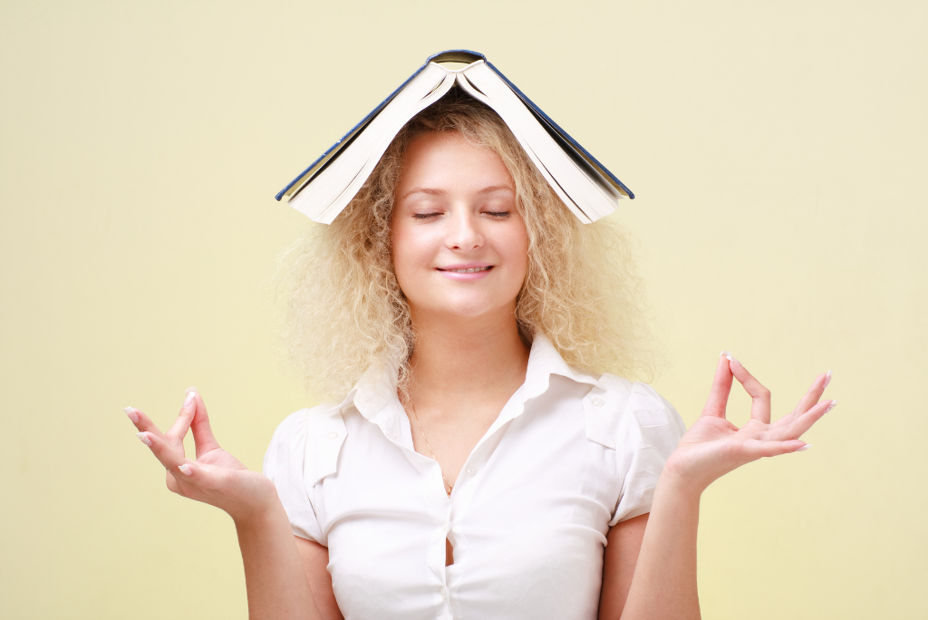 Smiling woman with a book on her head and eyes closed in a meditative pose.