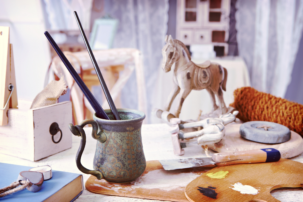 Artist's desk with paintbrushes, a palette, and a wooden horse sculpture.