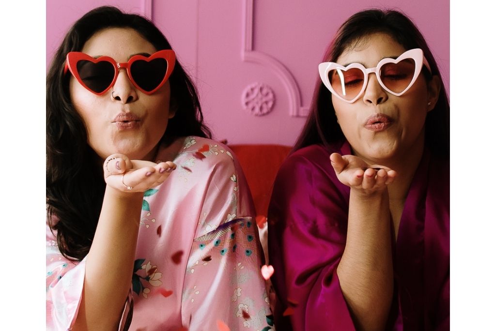 Two happy friends in heart-shaped glasses blowing kisses, celebrating Galentine's Day with Once Upon A Book Club.