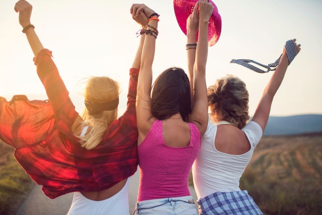 Three friends joyfully raising their arms in the sunset, embodying the spirit of Galentine's Day with Once Upon a Book Club.