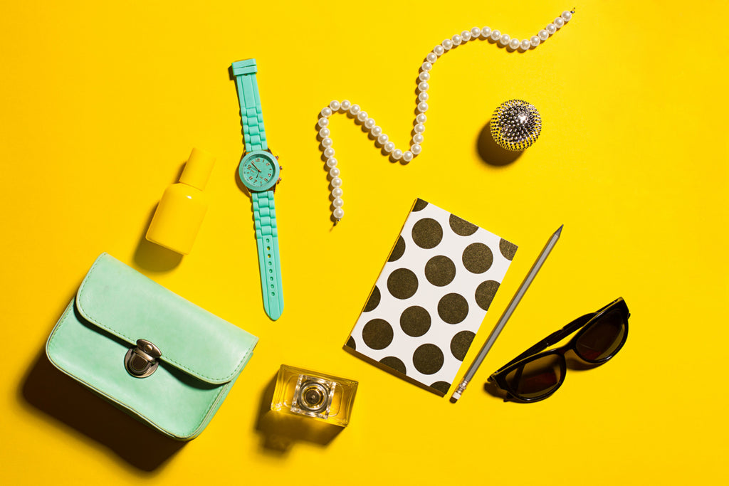 Flat lay of chic accessories: turquoise watch, pearls, notebook, on yellow.