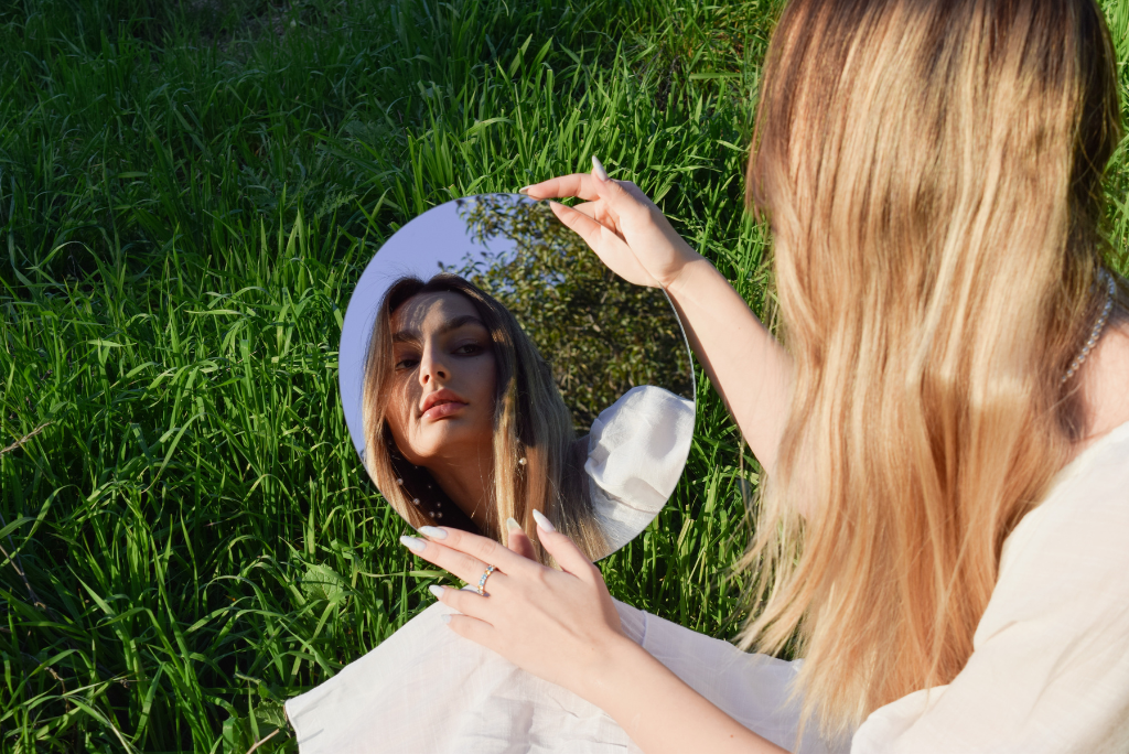 Woman holding a mirror reflecting her face in a grassy field.