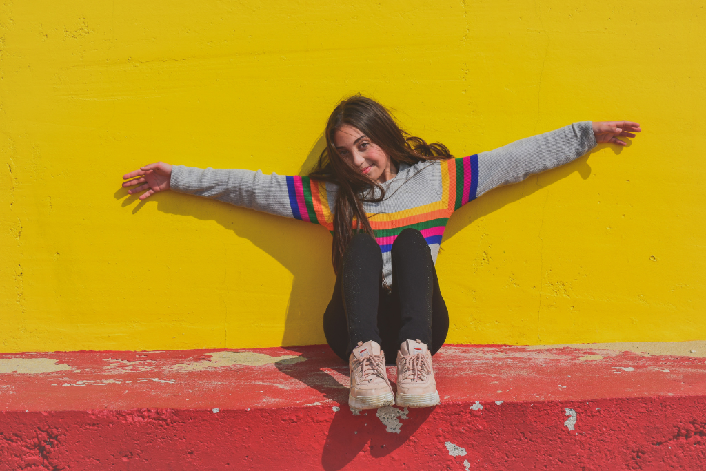 Cheerful girl stretching arms against a bright yellow and red wall.