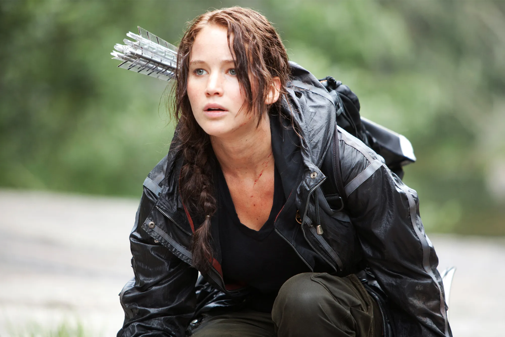 Katniss Everdeen in a black jacket with arrows on her back looks anxiously to the side