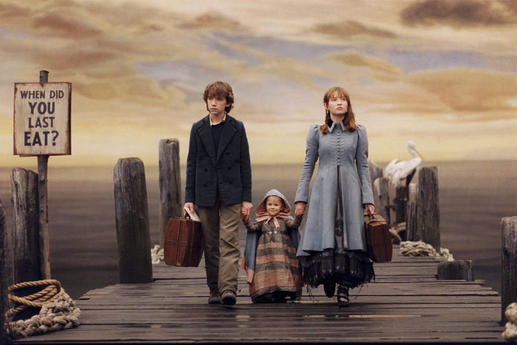A Series of Unfortunate Events - Three children with vintage attire on a desolate pier with a gloomy sky