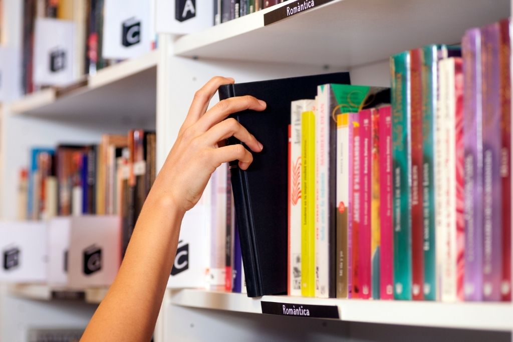 A hand selecting a book from a shelf filled with colorful titles in a cozy library setting.
