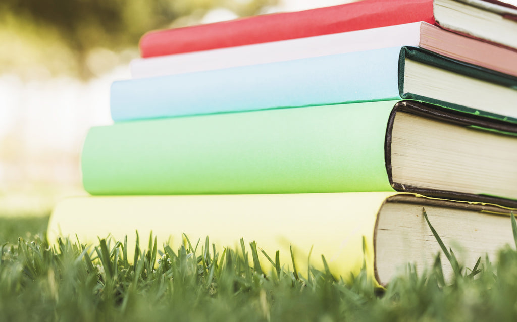 A stack of colorful books laid on grass, their spines creating a rainbow effect, symbolizing the joy of reading in nature.