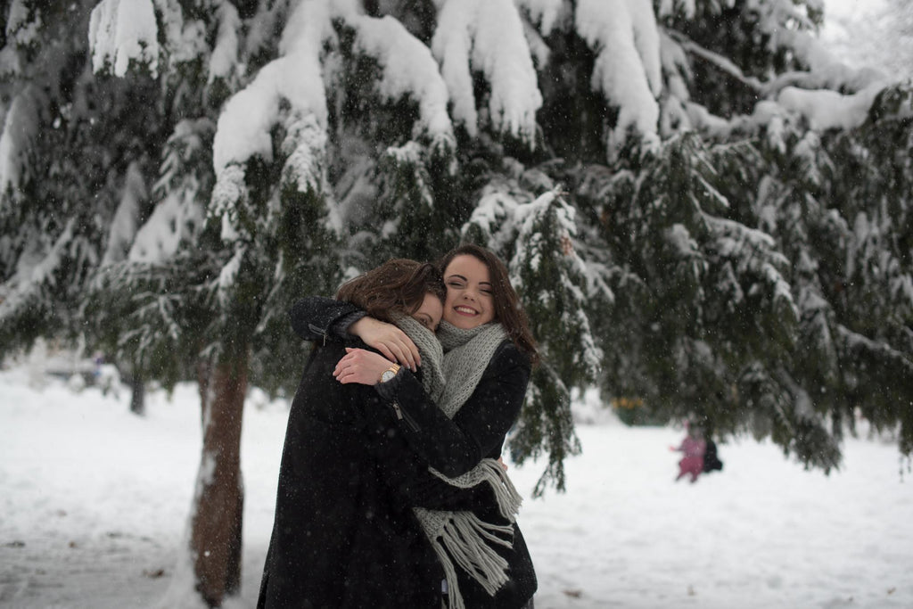 Two joyful women hugging in a snowy forest with trees laden with snow.