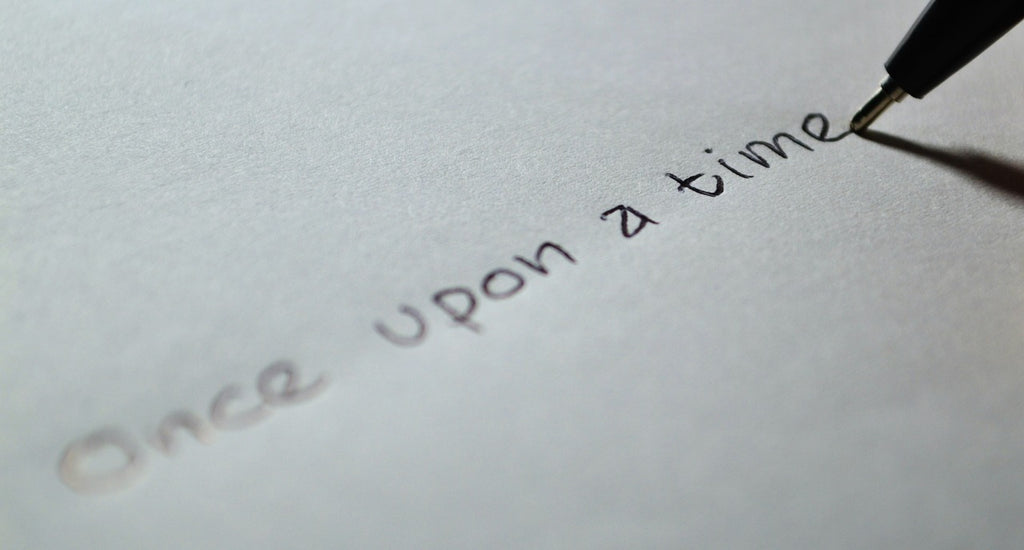 Close-up of a hand writing 'Once upon a time' with a fountain pen on a white paper, symbolizing the beginning of a creative story.