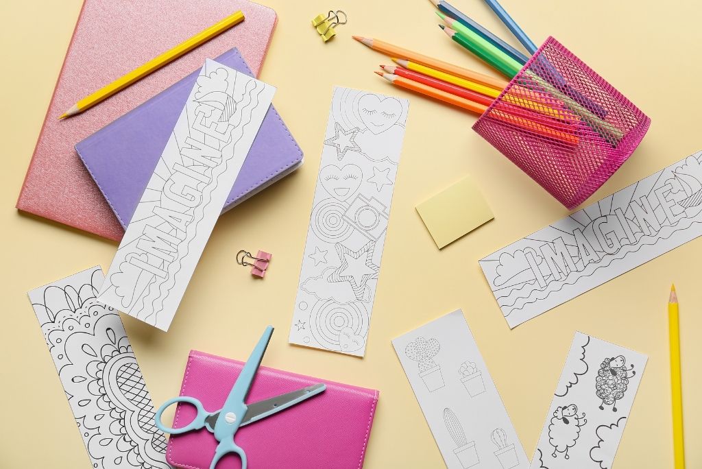 A vibrant array of coloring bookmarks, pencils, notebooks, and scissors arranged on a pastel yellow background for crafting.