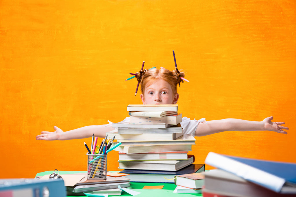 Young girl with arms outstretched behind a stack of books on a desk.