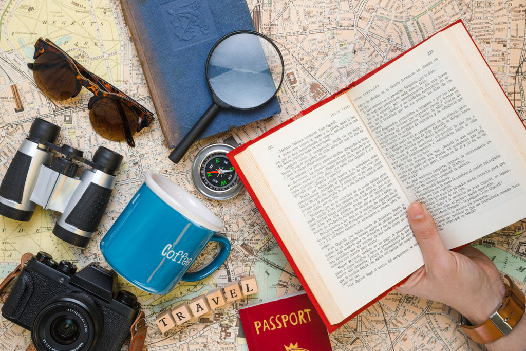 Flat lay of travel essentials with a book, suggesting a theme of traveling through reading.