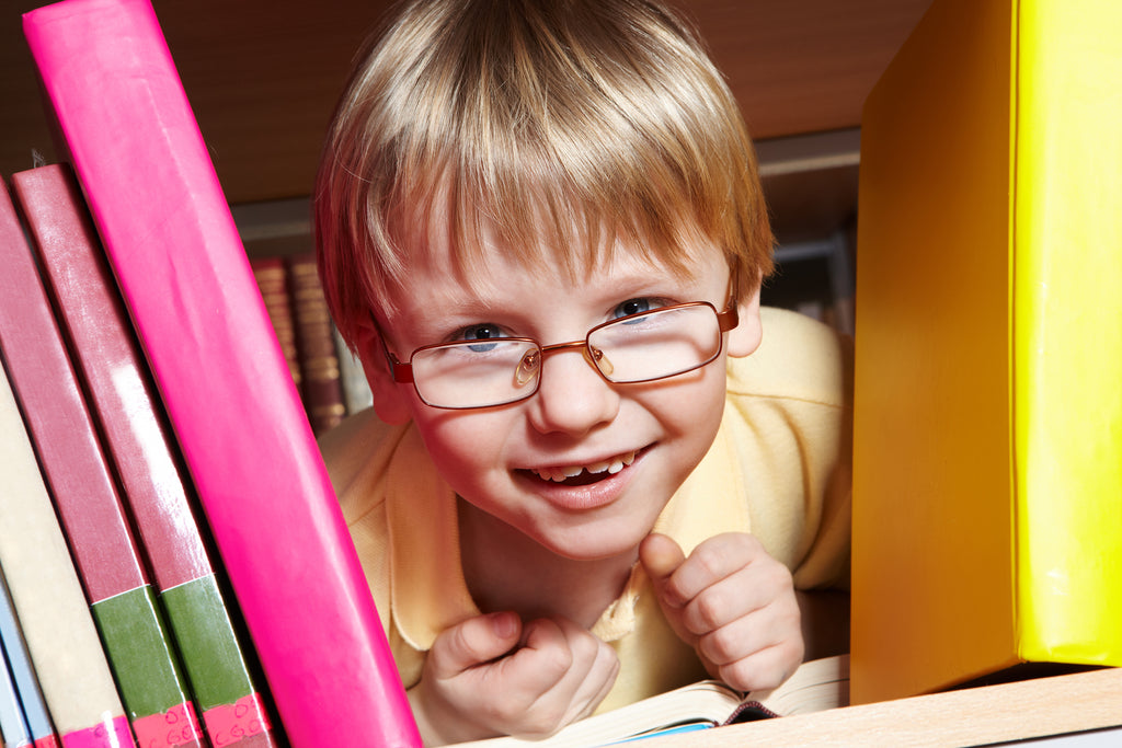 A cheerful young boy with glasses peeks through a gap in a bookshelf, his smile expressing delight and curiosity, symbolizing the joy of exploring the world of books.