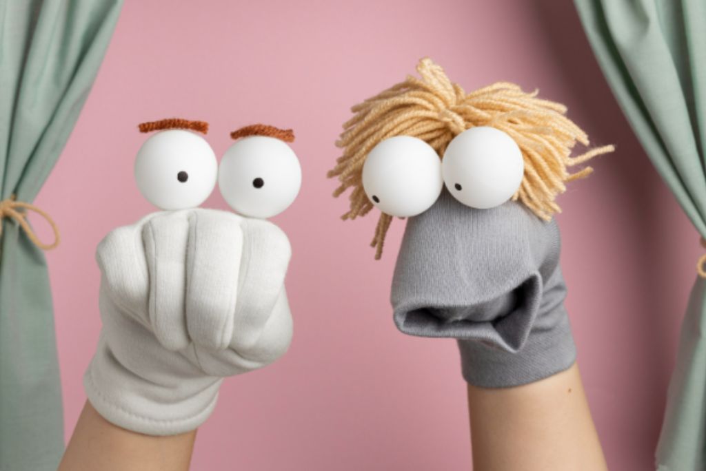Hand puppets with white spherical heads and yarn hair against a pink backdrop.
