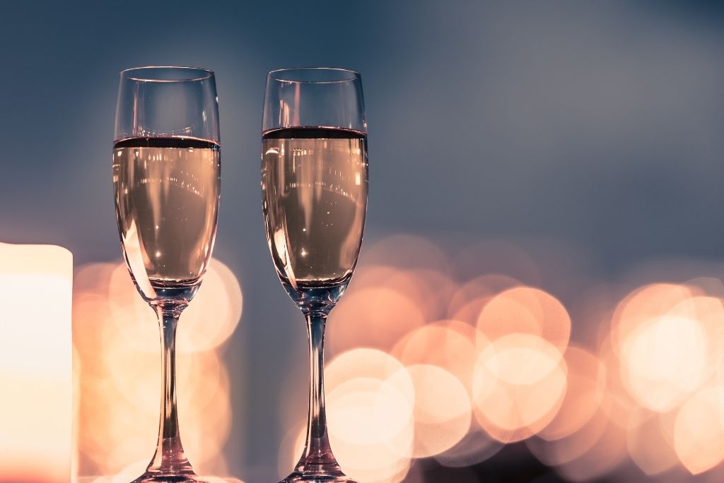 Two champagne glasses against a romantic, bokeh light backdrop, evoking an intimate celebration.