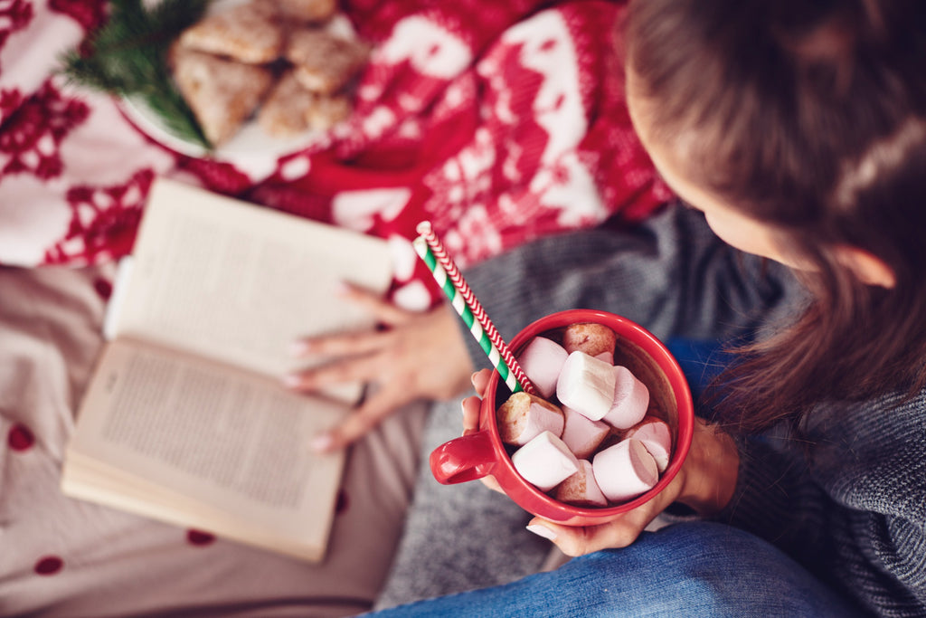 Woman enjoying a book and hot cocoa with marshmallows during holidays.