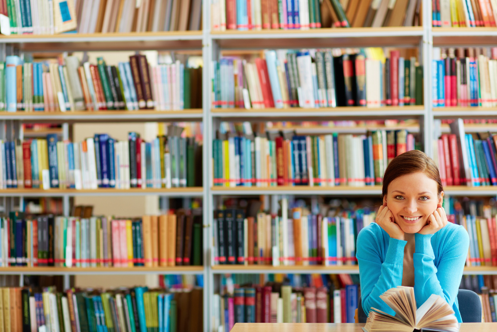 Smiling woman sitting with a book in a library.