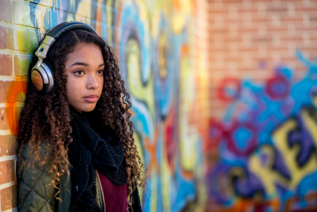 Teen with headphones against a graffiti wall.