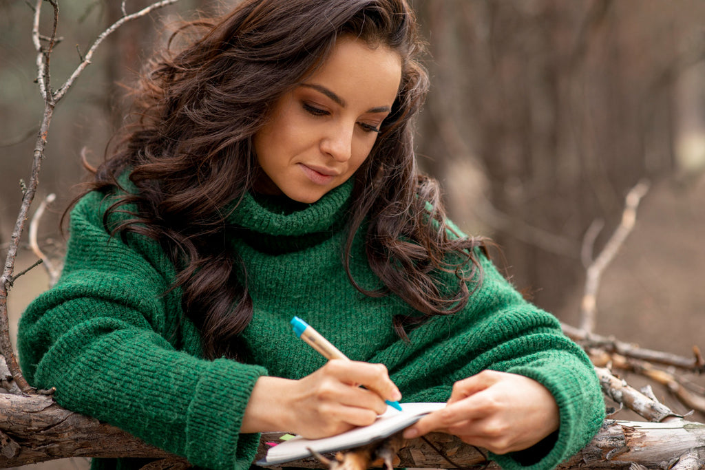 Woman in green sweater writing in notebook outdoors.