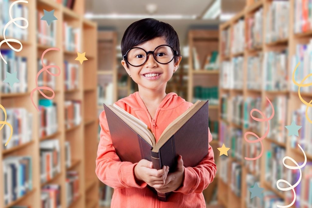 Happy child in glasses holding a book with a library background and festive streamers.