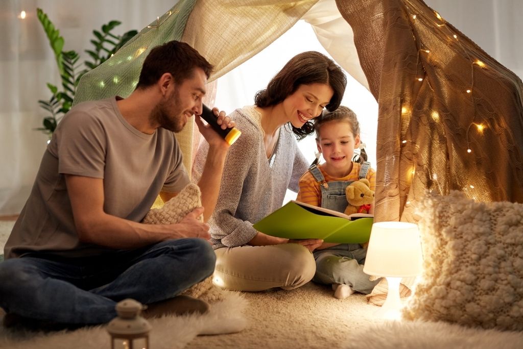 Family reading together inside a cozy blanket fort with warm fairy lights.