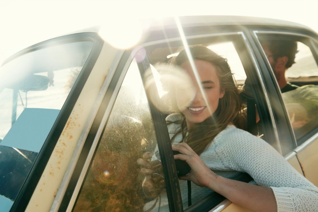 Happy woman leaning out of a car window, enjoying the ride with sunlight flaring around her.
