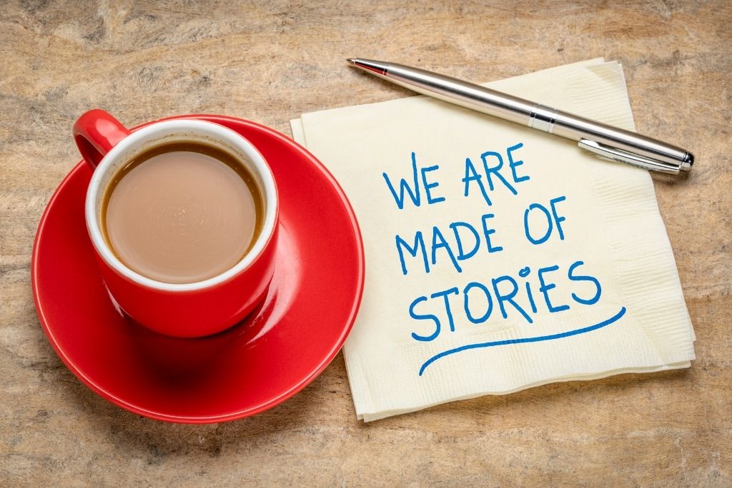 A cup of coffee with a napkin stating "WE ARE MADE OF STORIES" and a pen, on a wooden surface.