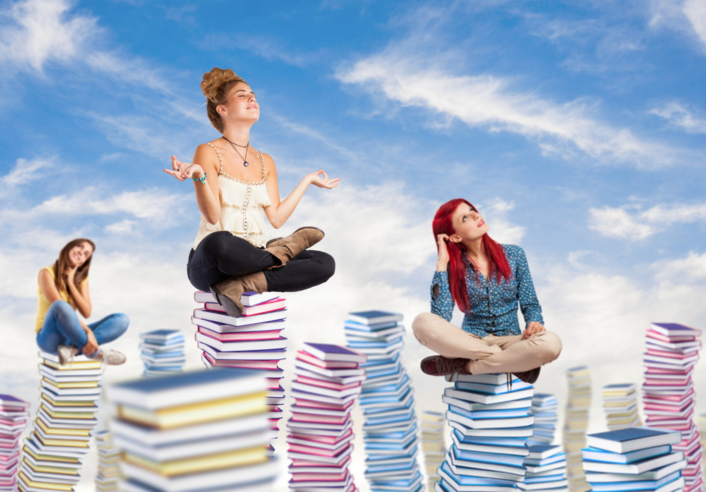 Three people sitting atop stacks of books against a sky backdrop, depicting relaxation and imagination.