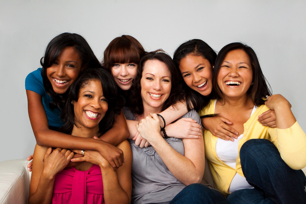 A group of six diverse women laughing and embracing, sharing a joyful moment together.