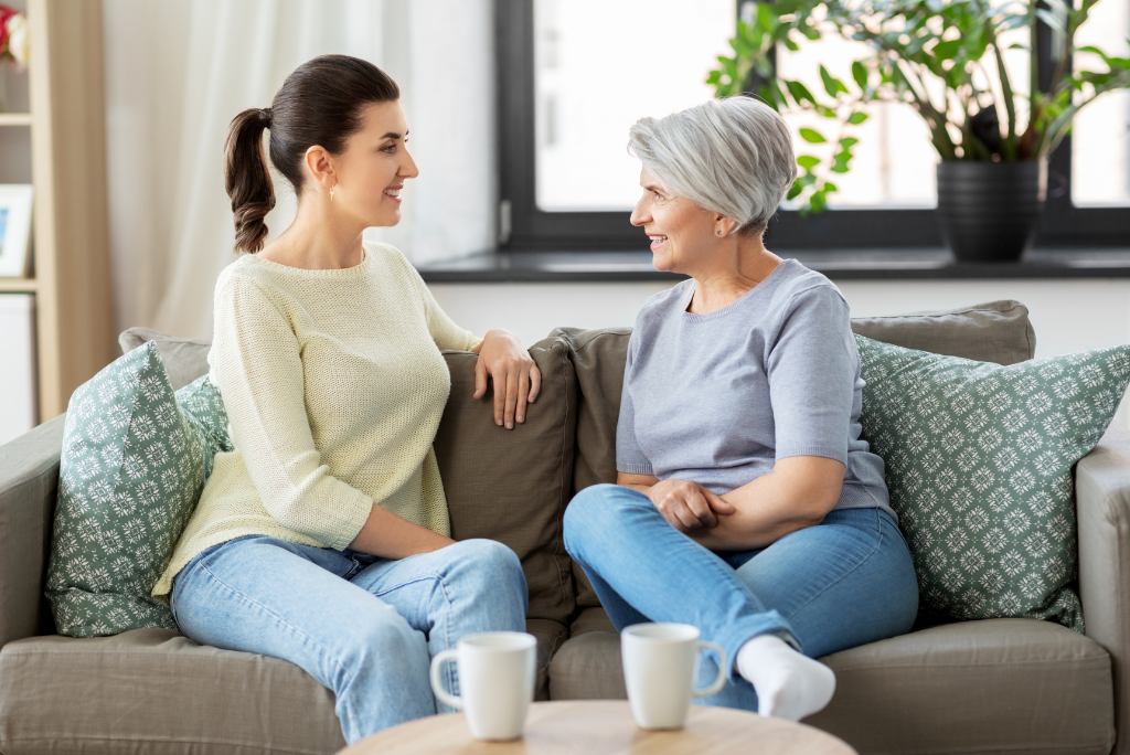 A young woman and an older woman with gray hair smiling and chatting on a sofa.