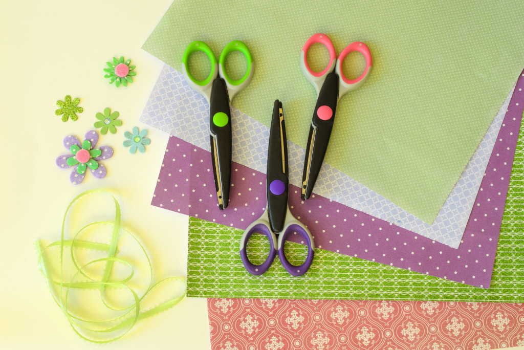 Crafting scissors, ribbons, and decorative paper on a yellow background.