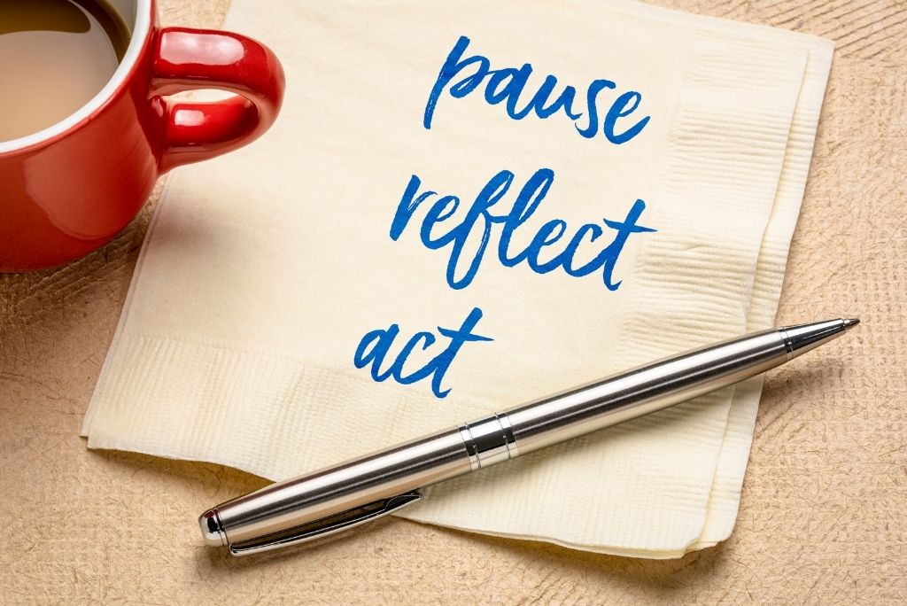 A red coffee mug beside a napkin with "pause reflect act" written on it, and a sleek pen, suggesting contemplation after reading.