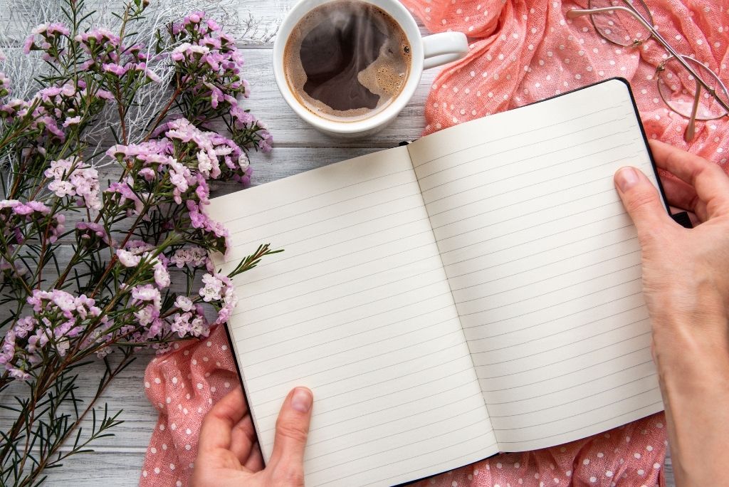 Open notebook with empty pages ready for reflective writing, next to a cup of coffee and fresh flowers, inspiring creativity.