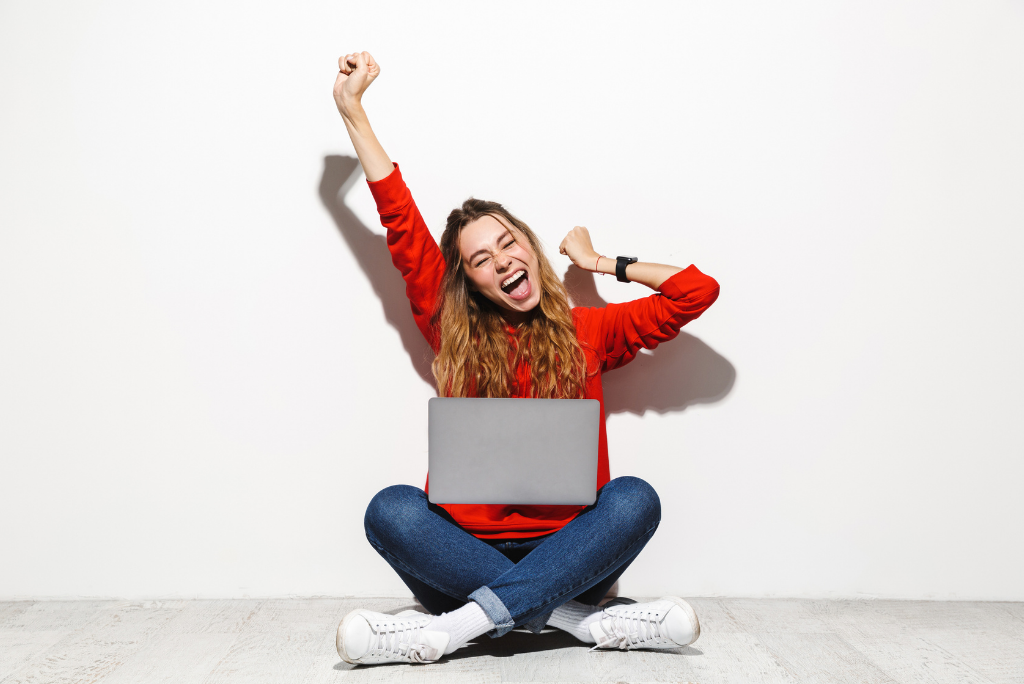 Exuberant woman in red shirt cheering with a laptop on the floor.
