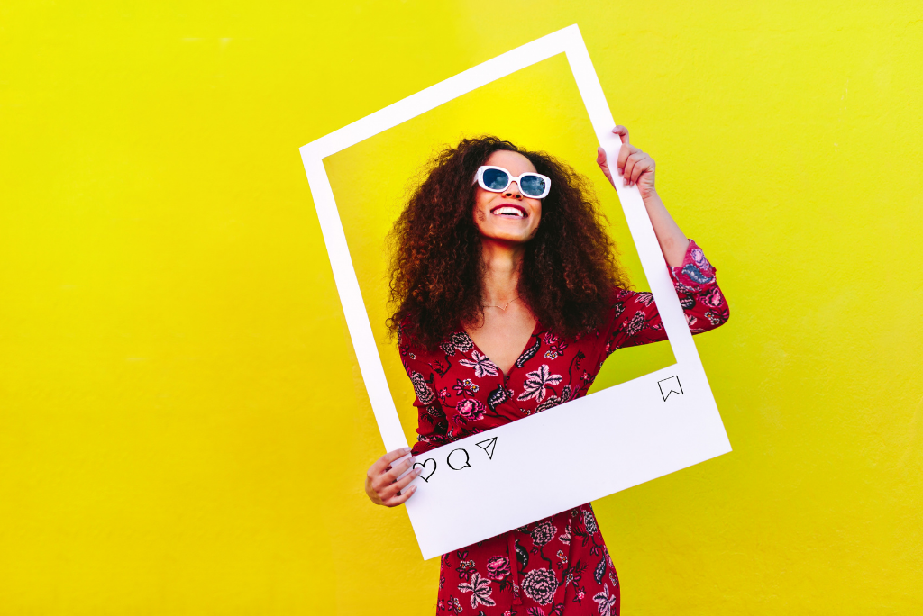 Joyful woman holding a social media-like frame against a yellow wall.